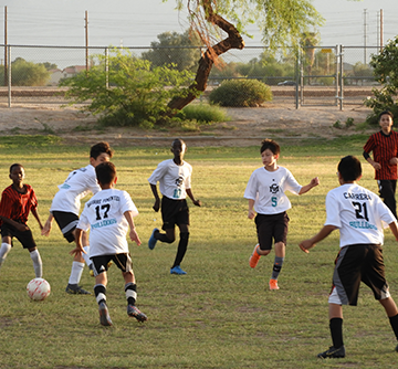 Male students play soccer together outside with another team