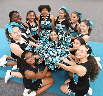 Cheerleaders pose in a circle with their pom poms