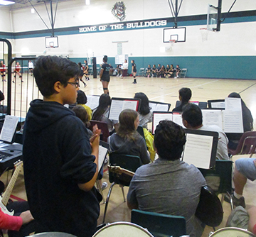 School band members watch a volleyball game in the gym