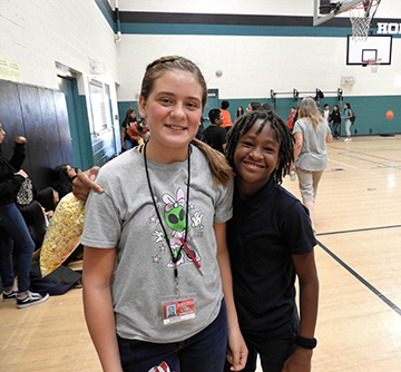 Two students pose together in the gym as one student holds a bag of popcorn