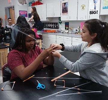 Two female students connect plastic straws together as part of a project in a classroom