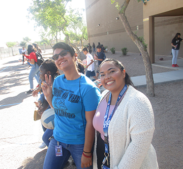 A smiling female student poses outside with a female student holding up a peace sign with her fingers
