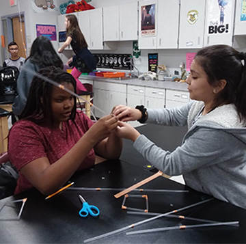 Two students connect plastic straws together as part of a project in a classroom